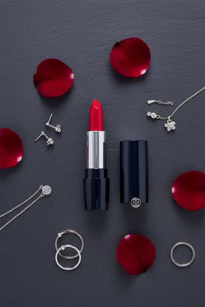 Flat lay of navy blue lipstick with rose petals and silver jewelry on dark slate