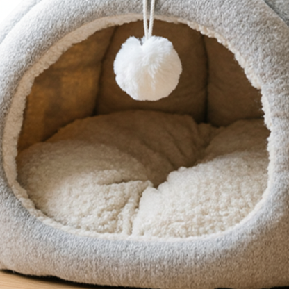 Cat cave interior close-up showing cream sherpa fleece cushion and hanging pompom toy